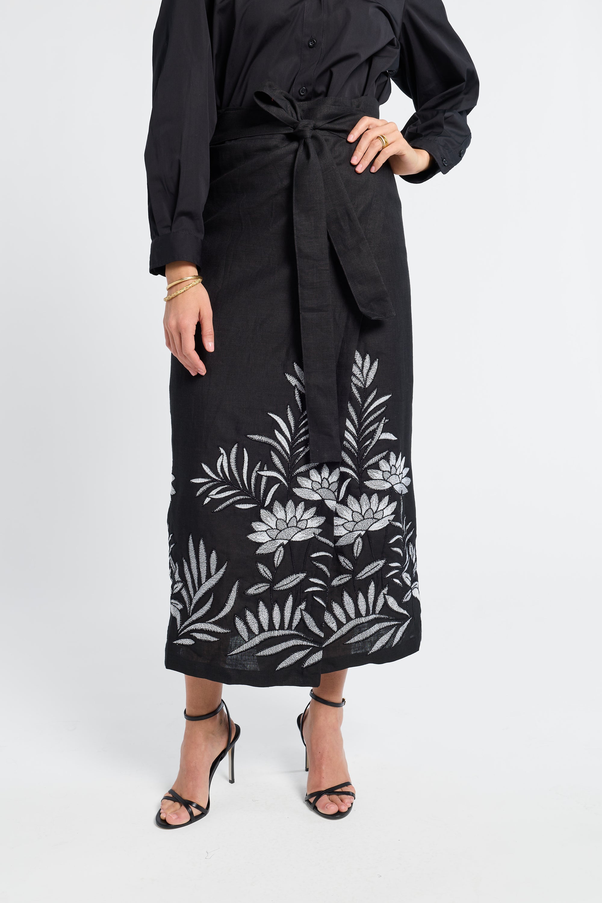 woman wearing a black pareo with floral embroidery and black heels on a white background