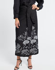 woman wearing a black pareo with floral embroidery and black heels on a white background