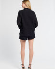 Person wearing a black blouse and shorts on a white backdrop