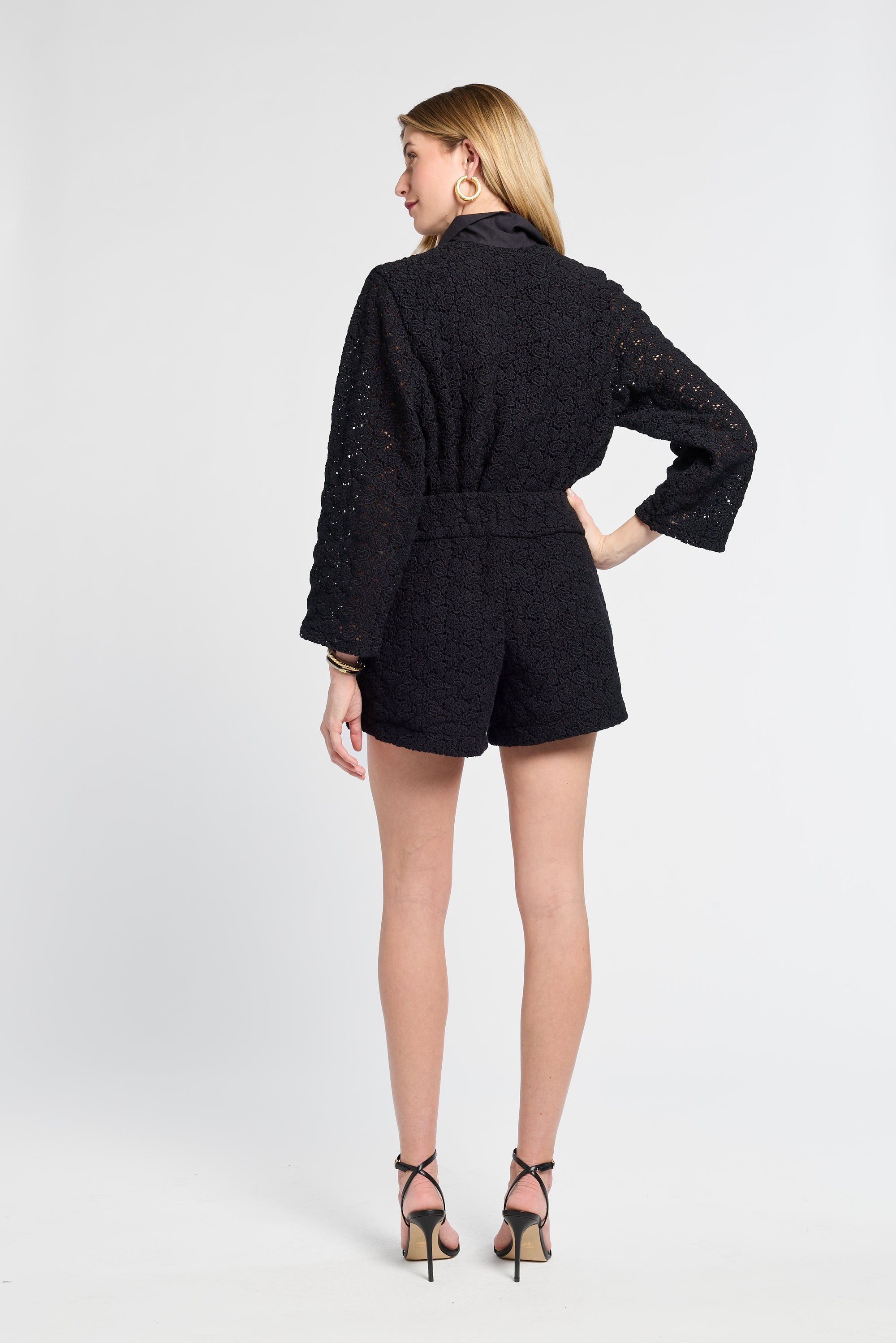 Woman wearing a black lace blouse and shorts white background