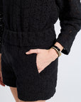 Person wearing a black lace blouse and shorts on a white background
