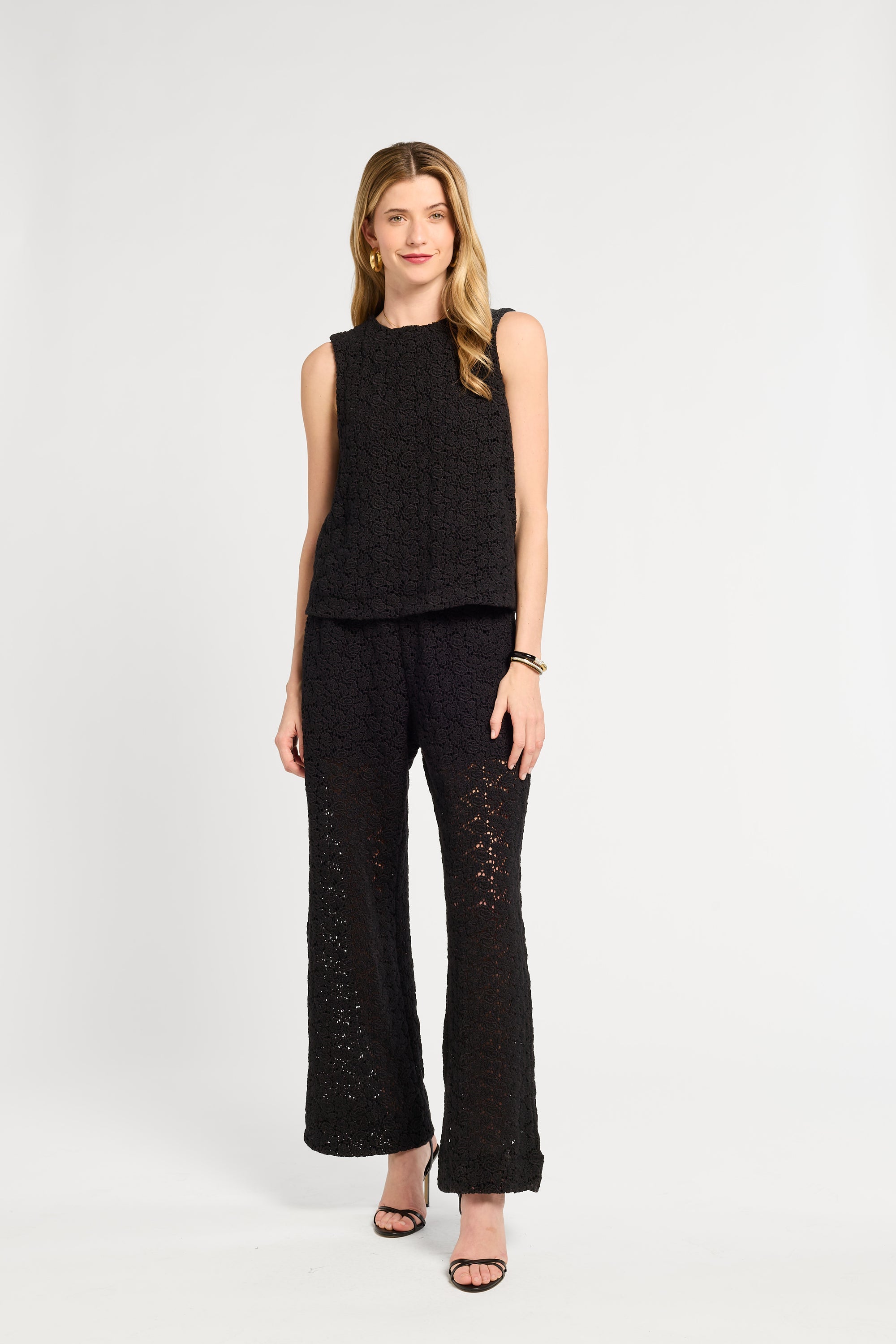 Woman wearing a black sleeveless blouse and wide-leg pants on a white background