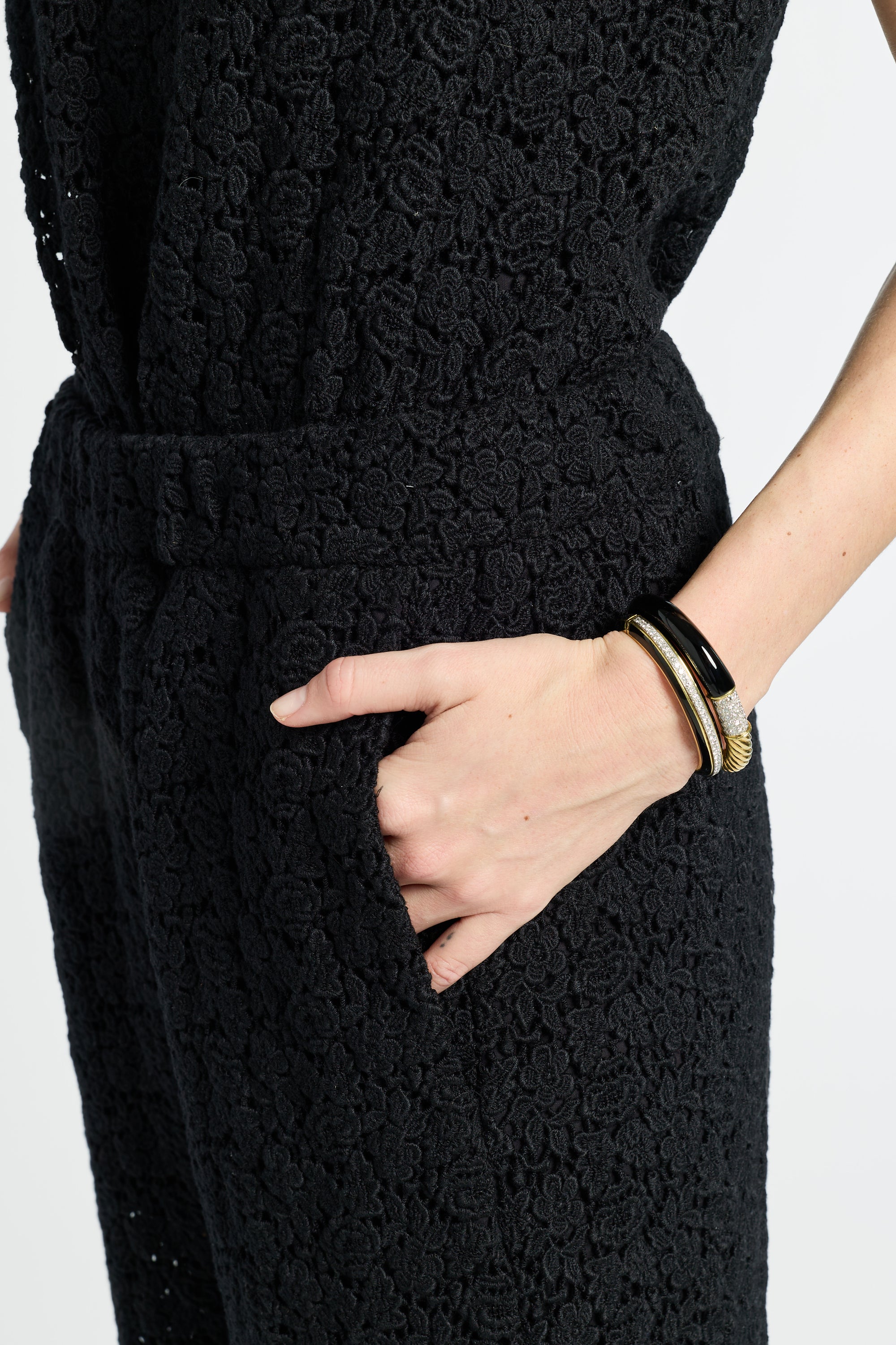 Person wearing a black floral textured outfit with hands in pockets on a white background