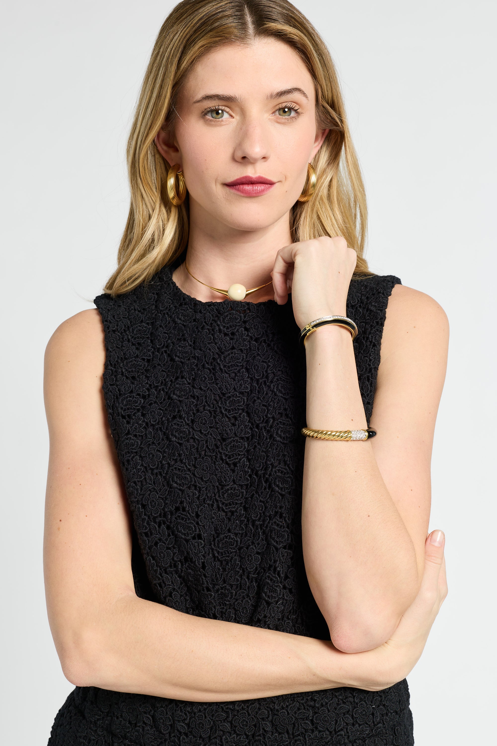 Woman wearing a black sleeveless blouse with gold jewelry on a white background