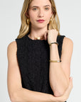 Woman wearing a black sleeveless blouse with gold jewelry on a white background