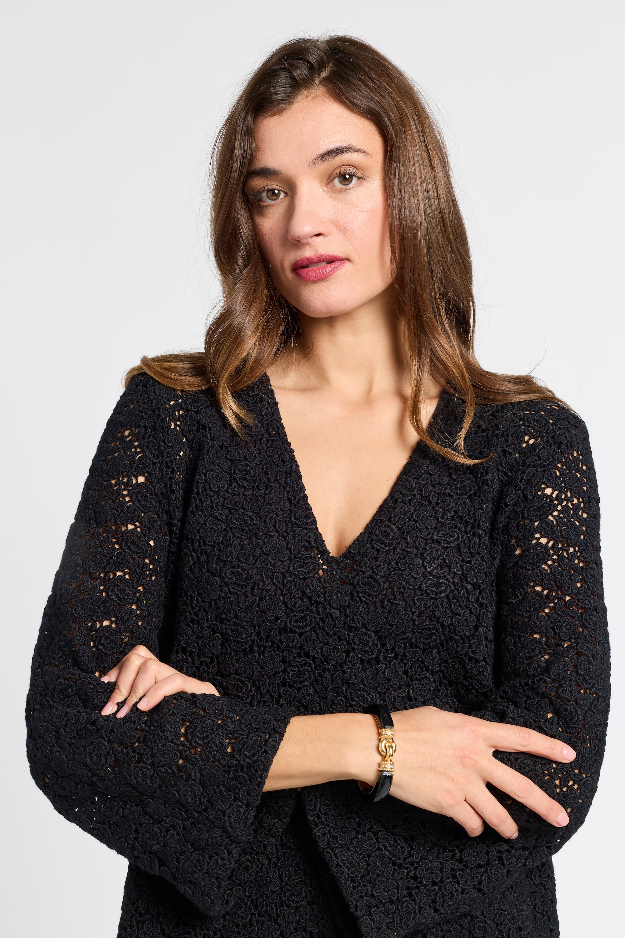 Woman wearing a black v-neck dress with gold jewelry on a white background