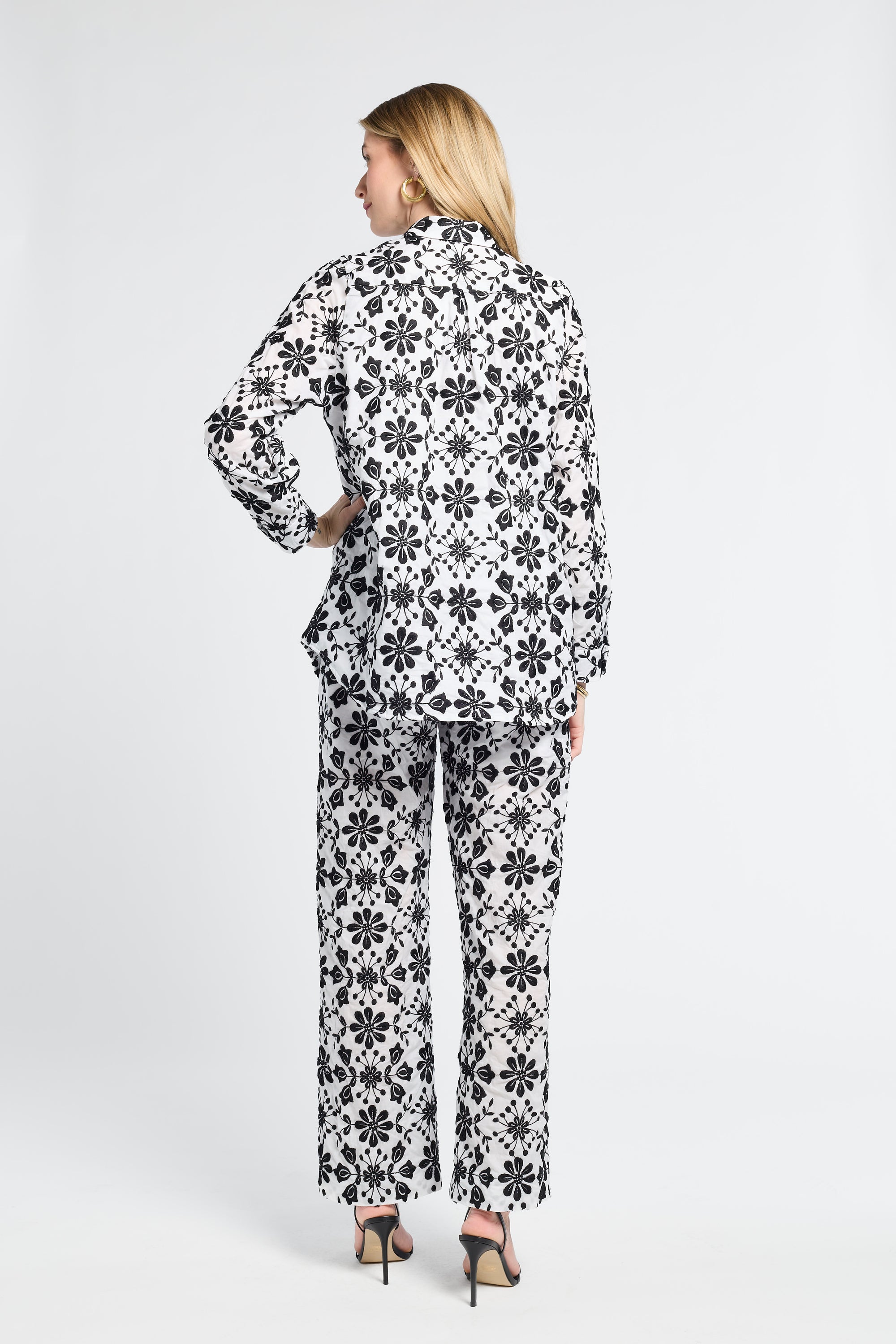 Woman wearing a black and white floral patterned blouse and pants with black heels on a white background
