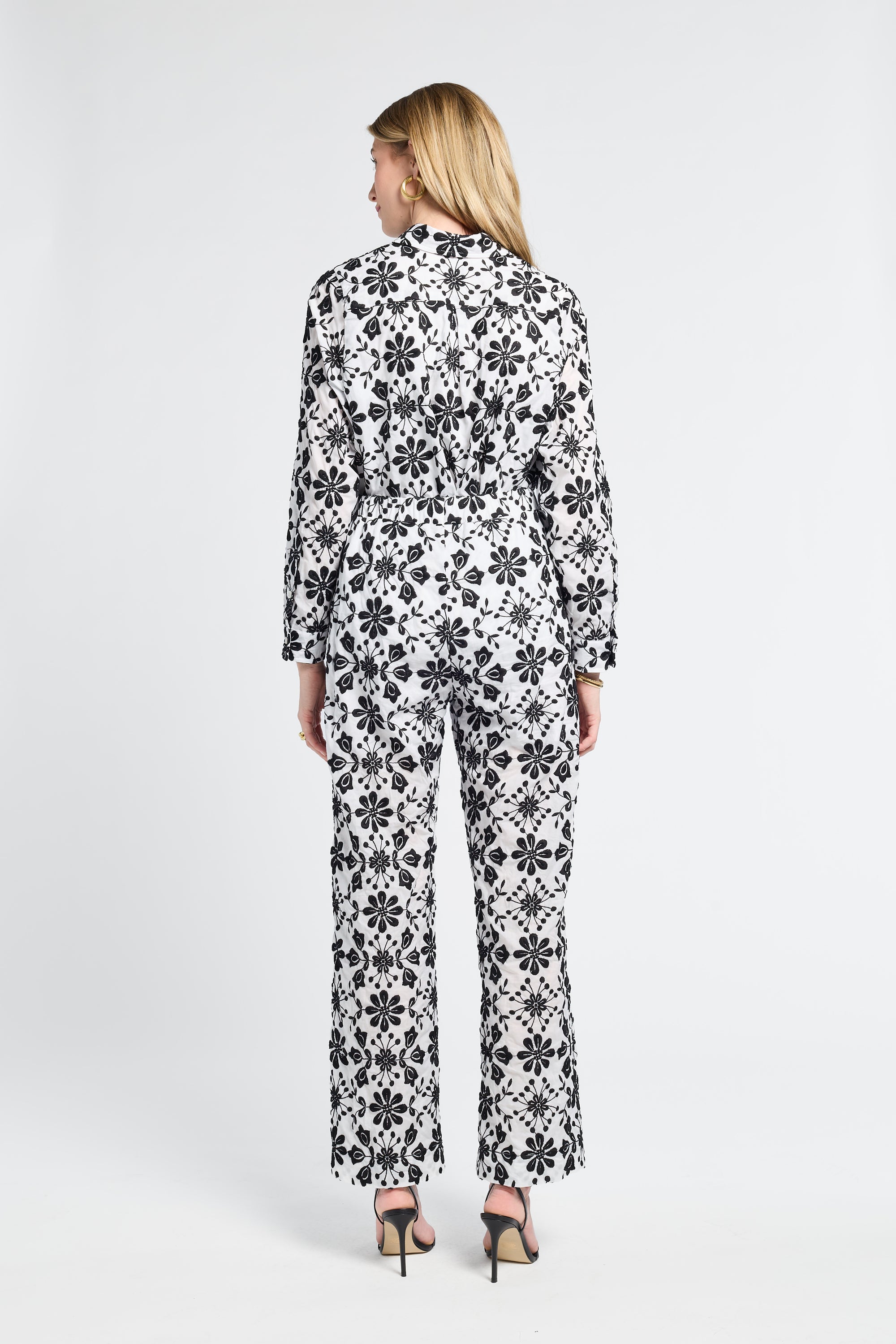 Woman wearing a black and white floral long sleeve blouse and long pants on a white background