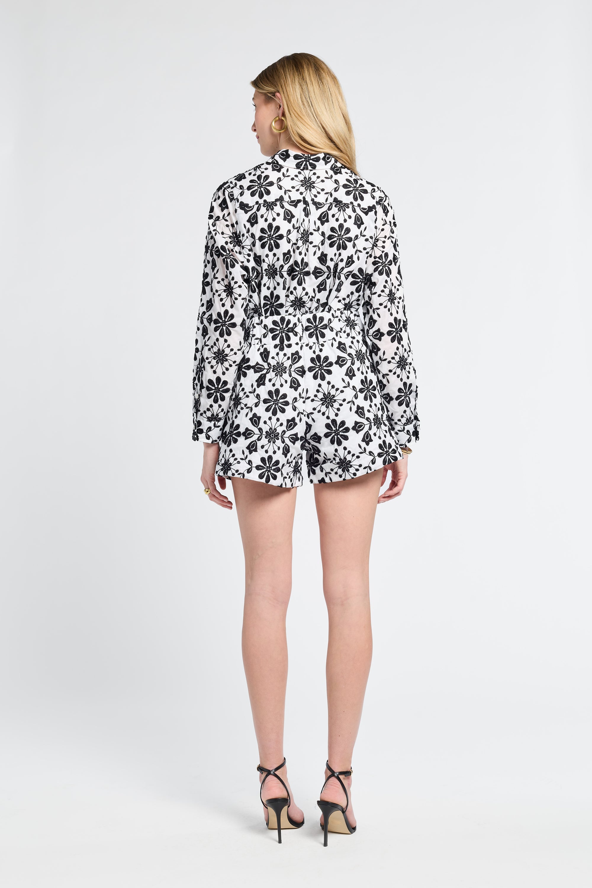 Woman modeling a black and white floral blouse with black heels on a white background