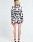 Woman modeling a black and white floral blouse with black heels on a white background