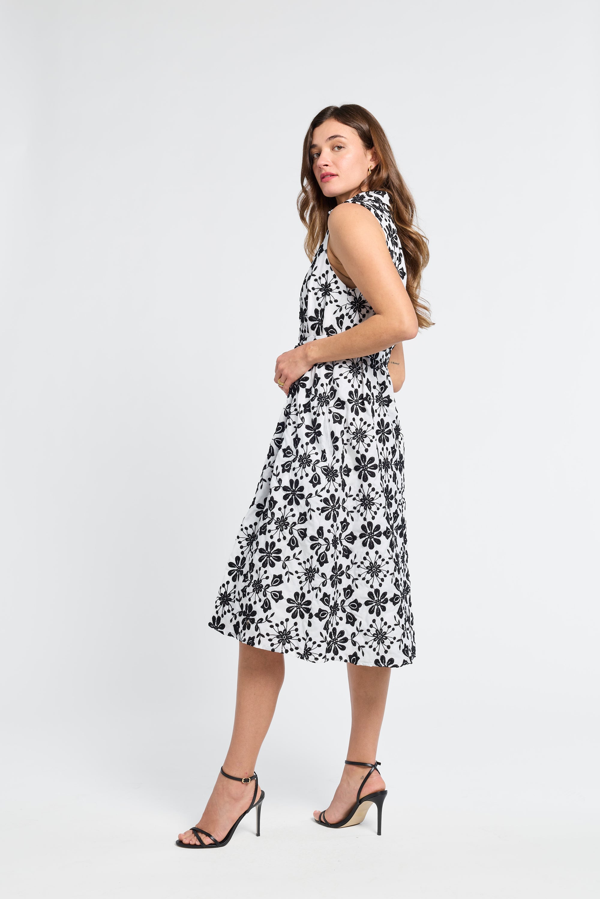 Woman wearing a black and white floral midi dress with black heels on a white background