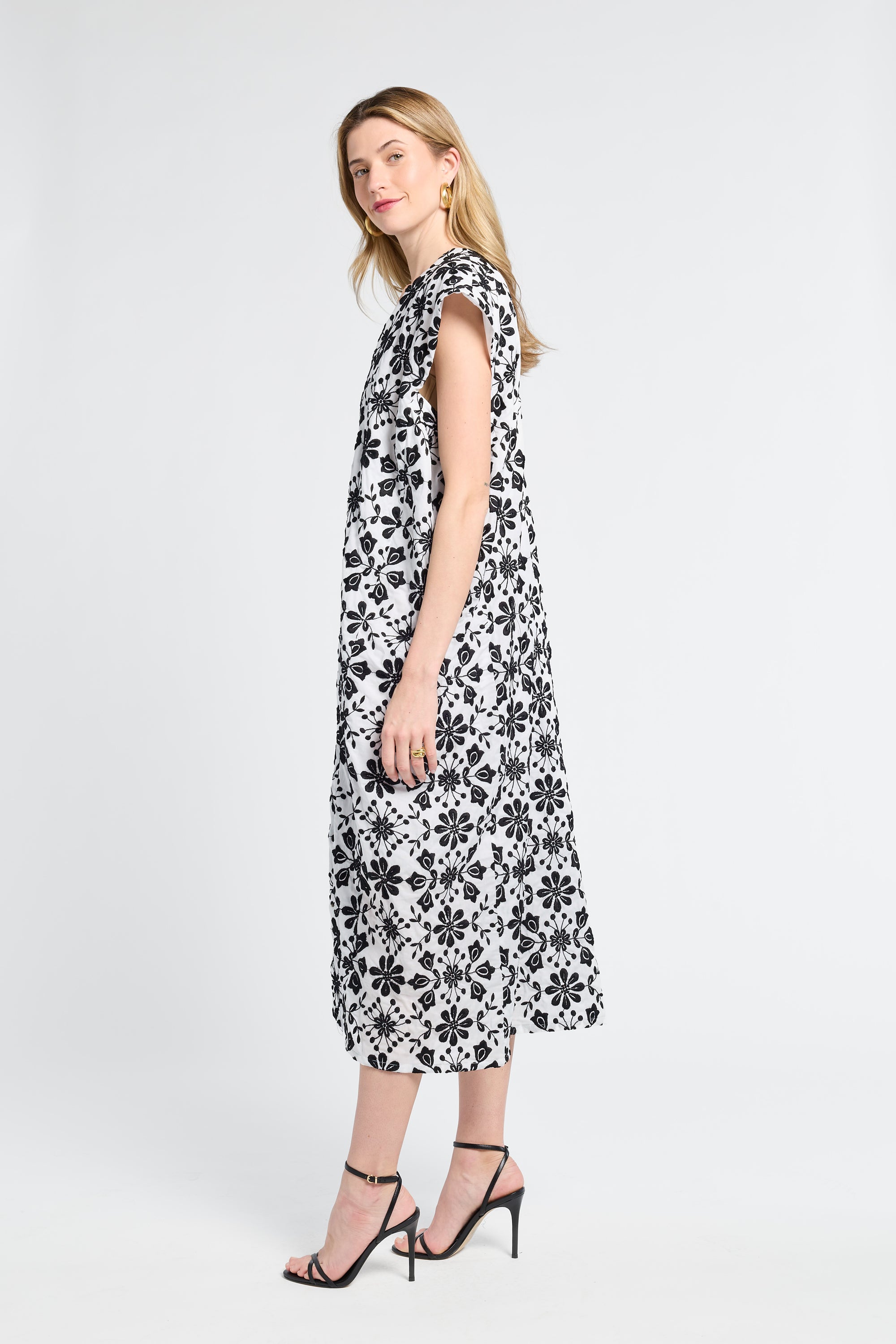 Woman wearing a black and white floral caftan and black heels on a white background