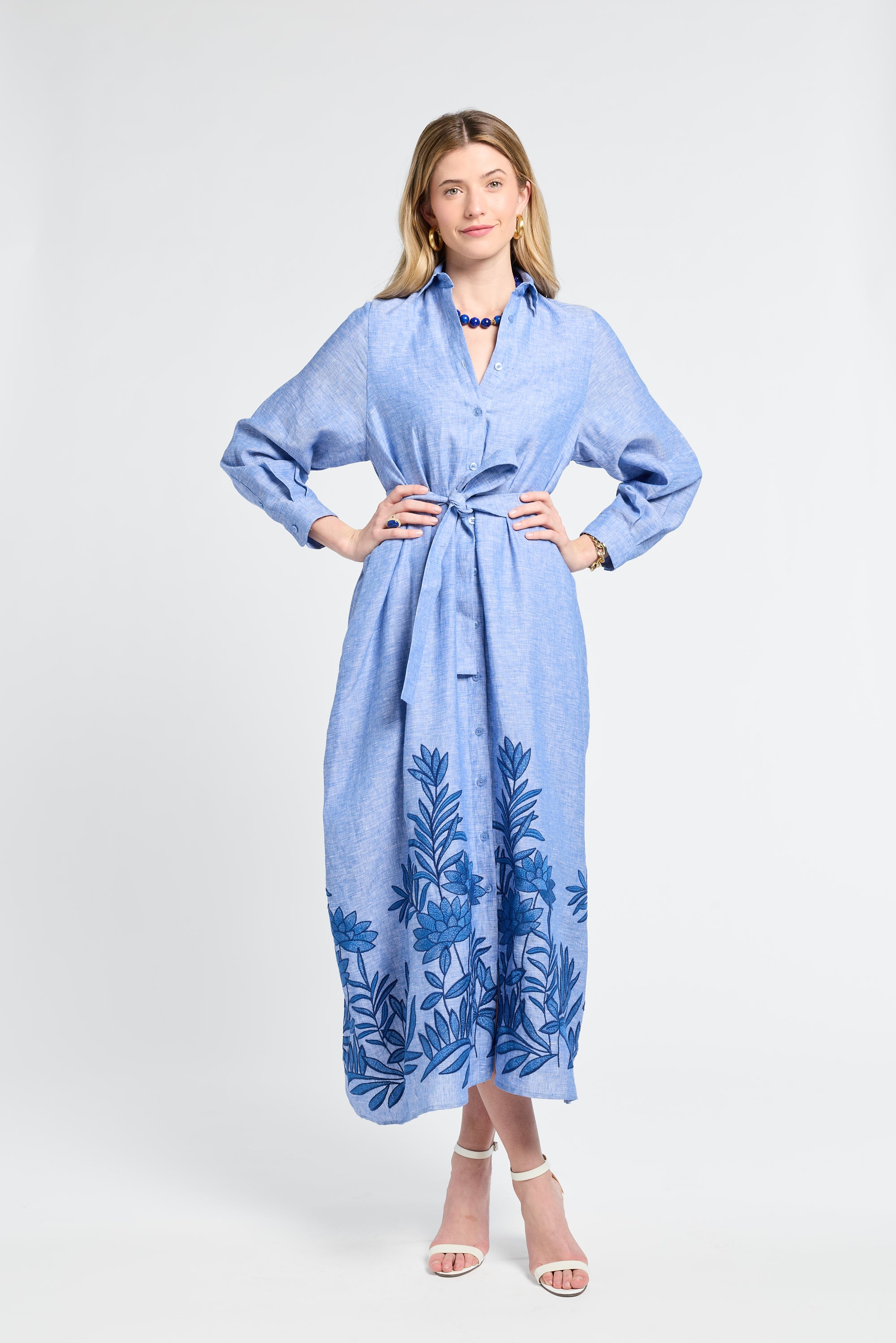 Woman wearing a blue maxi dress with floral embroidery on a white background