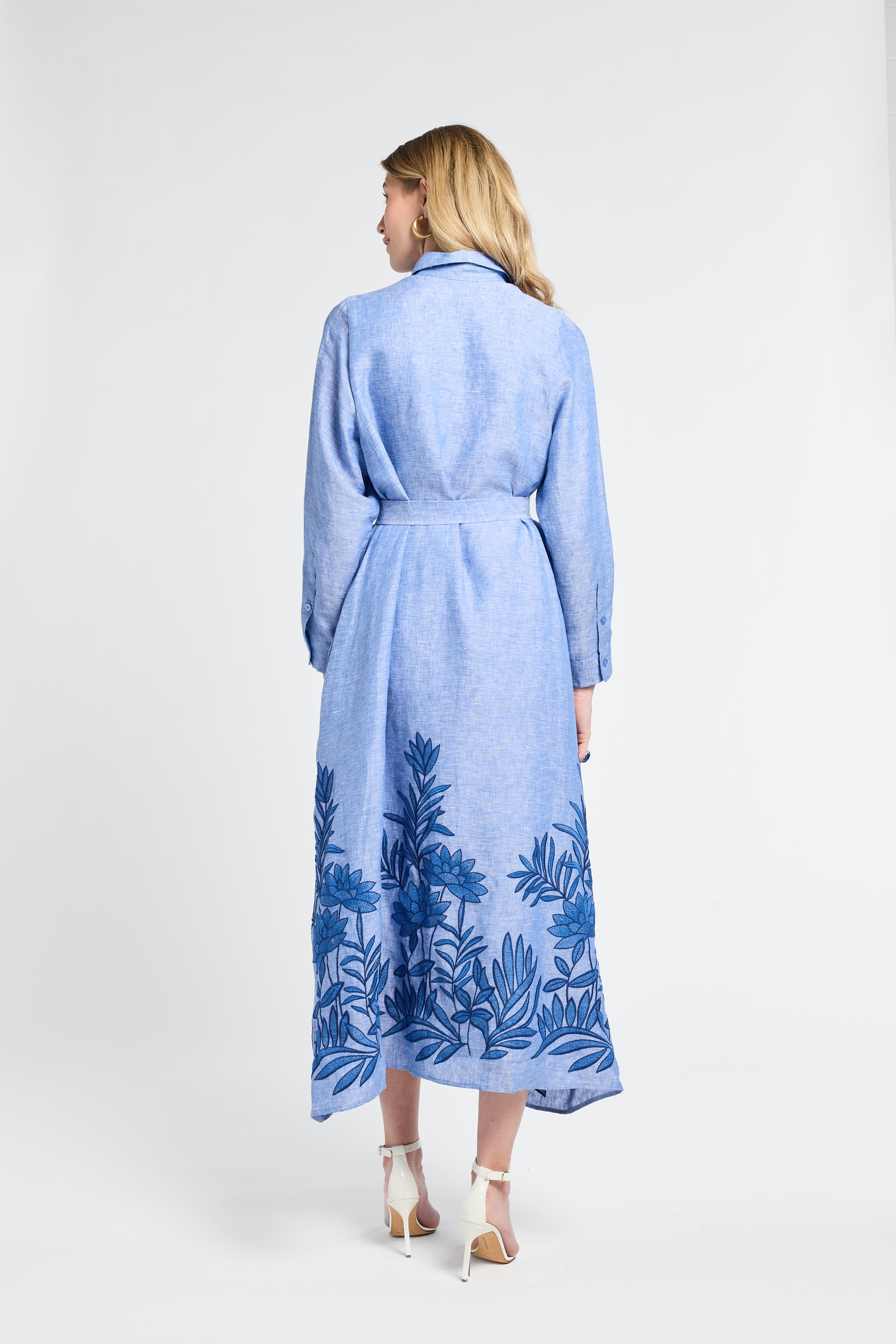 Woman wearing a long blue dress with floral embroidery on a white background