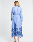 Woman wearing a long blue dress with floral embroidery on a white background