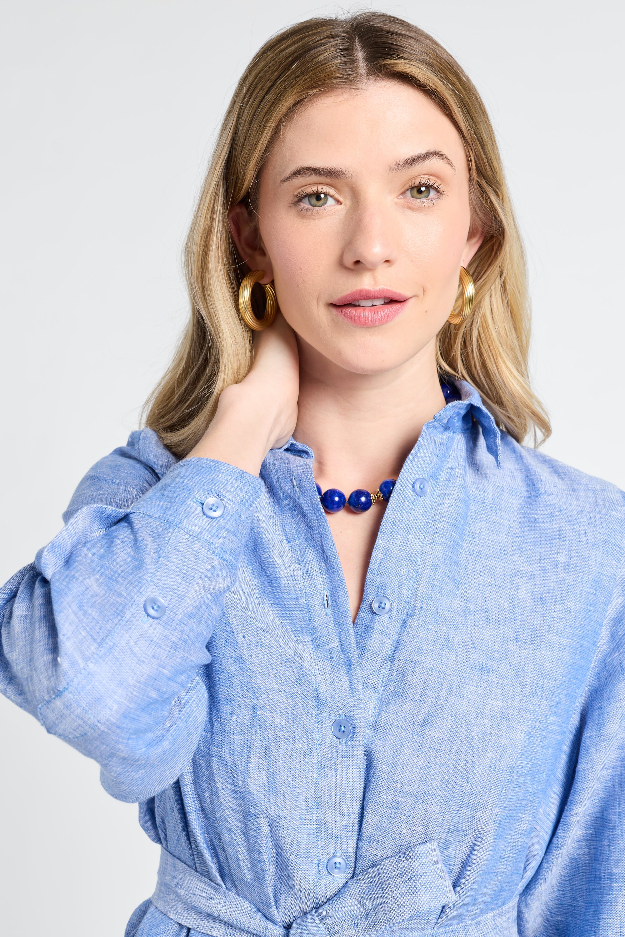 Woman wearing a button down blue dress and necklace with a plain background