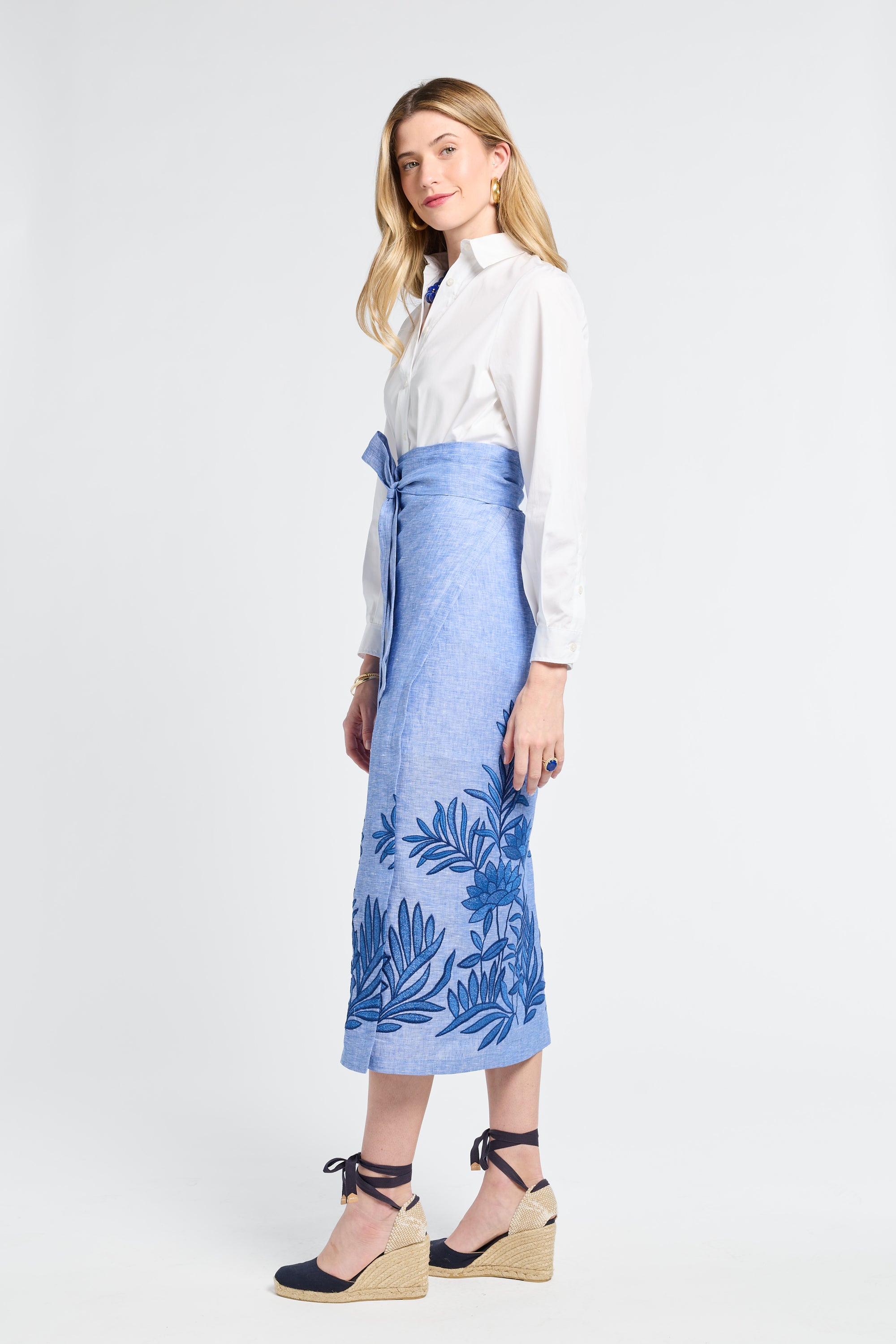 Woman wearing a white blouse and blue floral wrap skirt on a white background