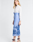 Woman wearing a white blouse and blue floral wrap skirt on a white background