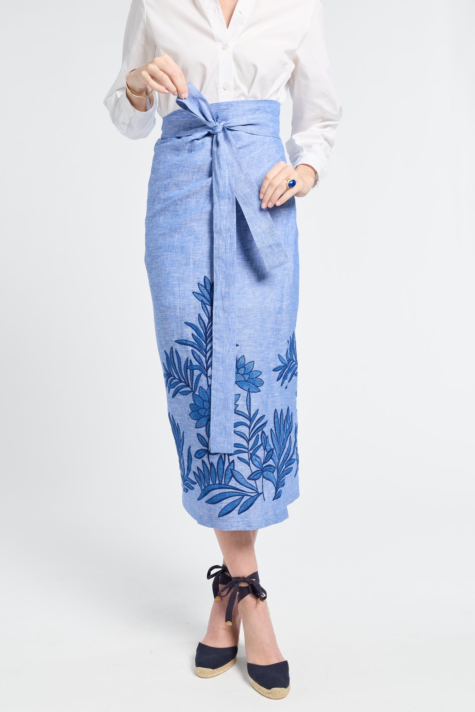 Woman modeling a blue skirt with floral embroidery on a white background