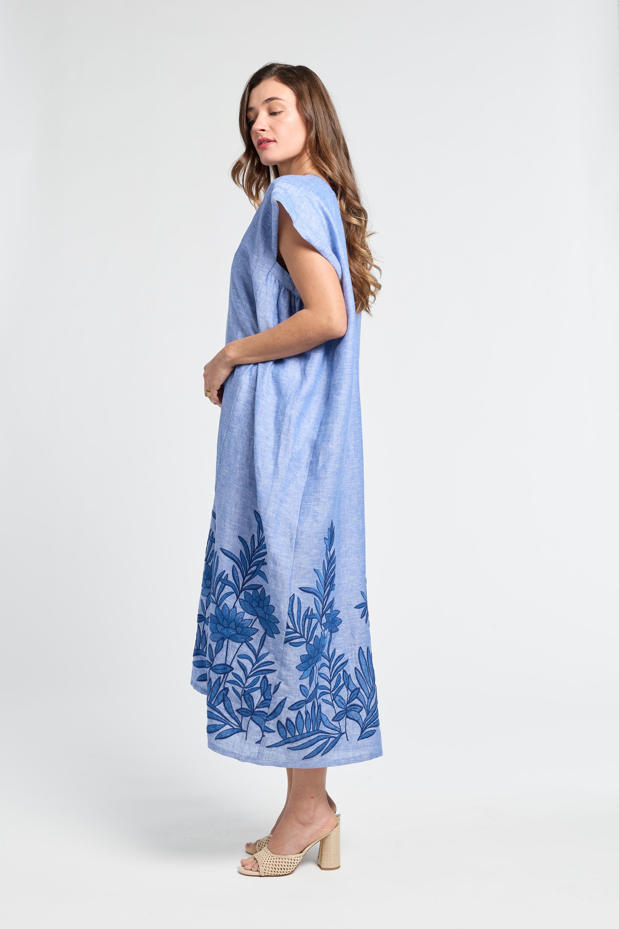 Woman wearing a long blue caftan with floral embroidery on a white background