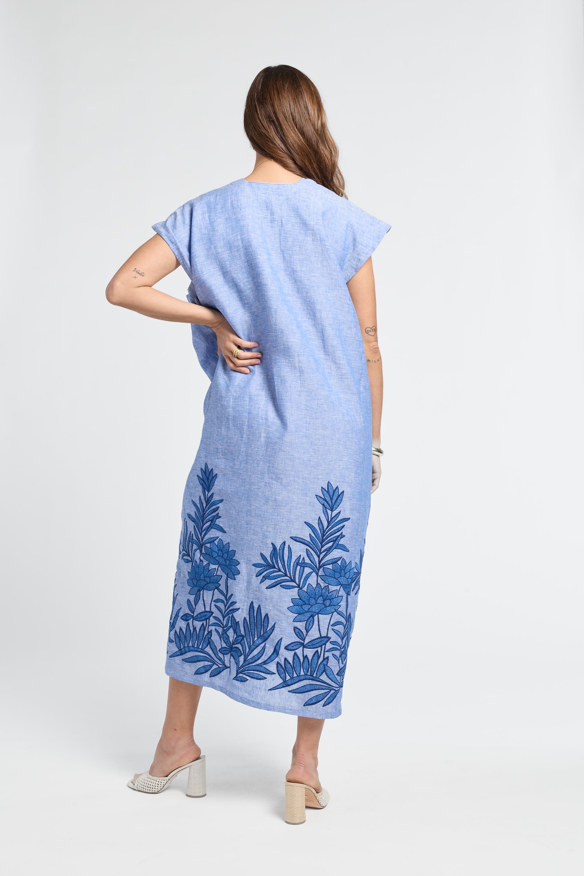 Woman wearing a blue dress with floral embroidery on a white backdrop