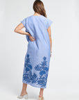 Woman wearing a blue dress with floral embroidery on a white backdrop