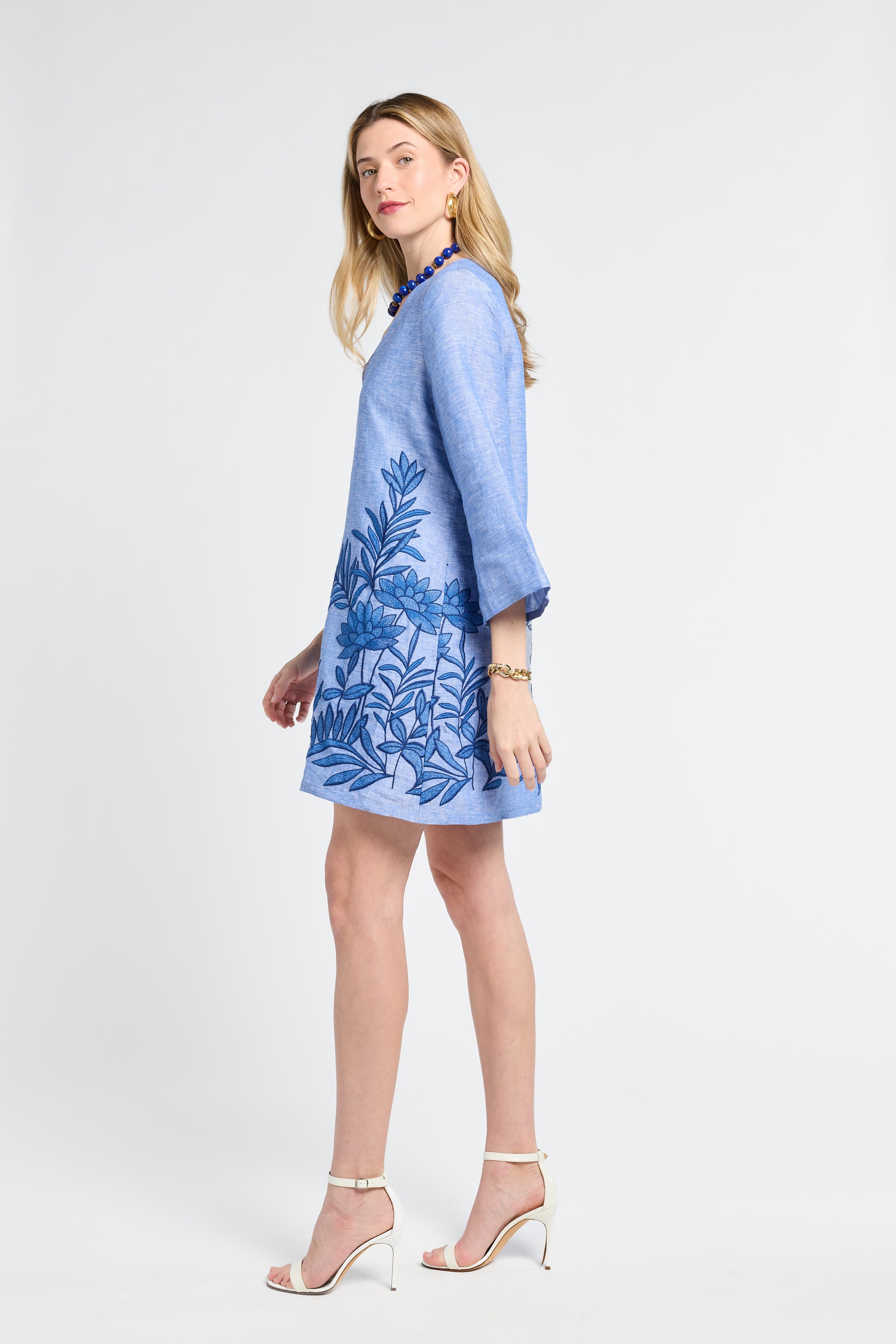 Woman wearing a blue caftan with floral embroidery with white heels on a white background