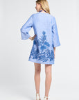 Woman wearing a mid length blue caftan with floral embroidery on a white background