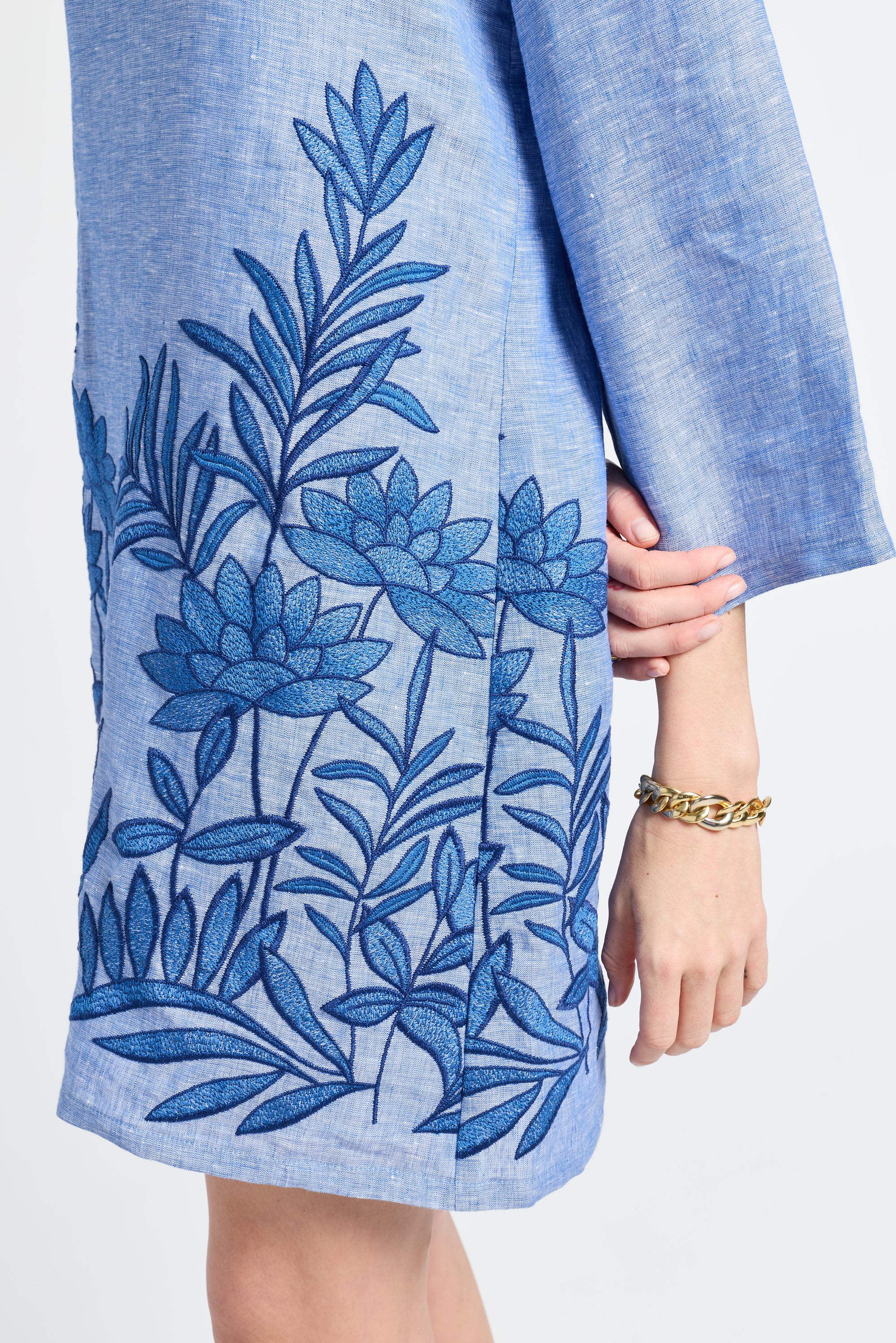 woman dressed in a blue caftan with floral embroidery on a white background