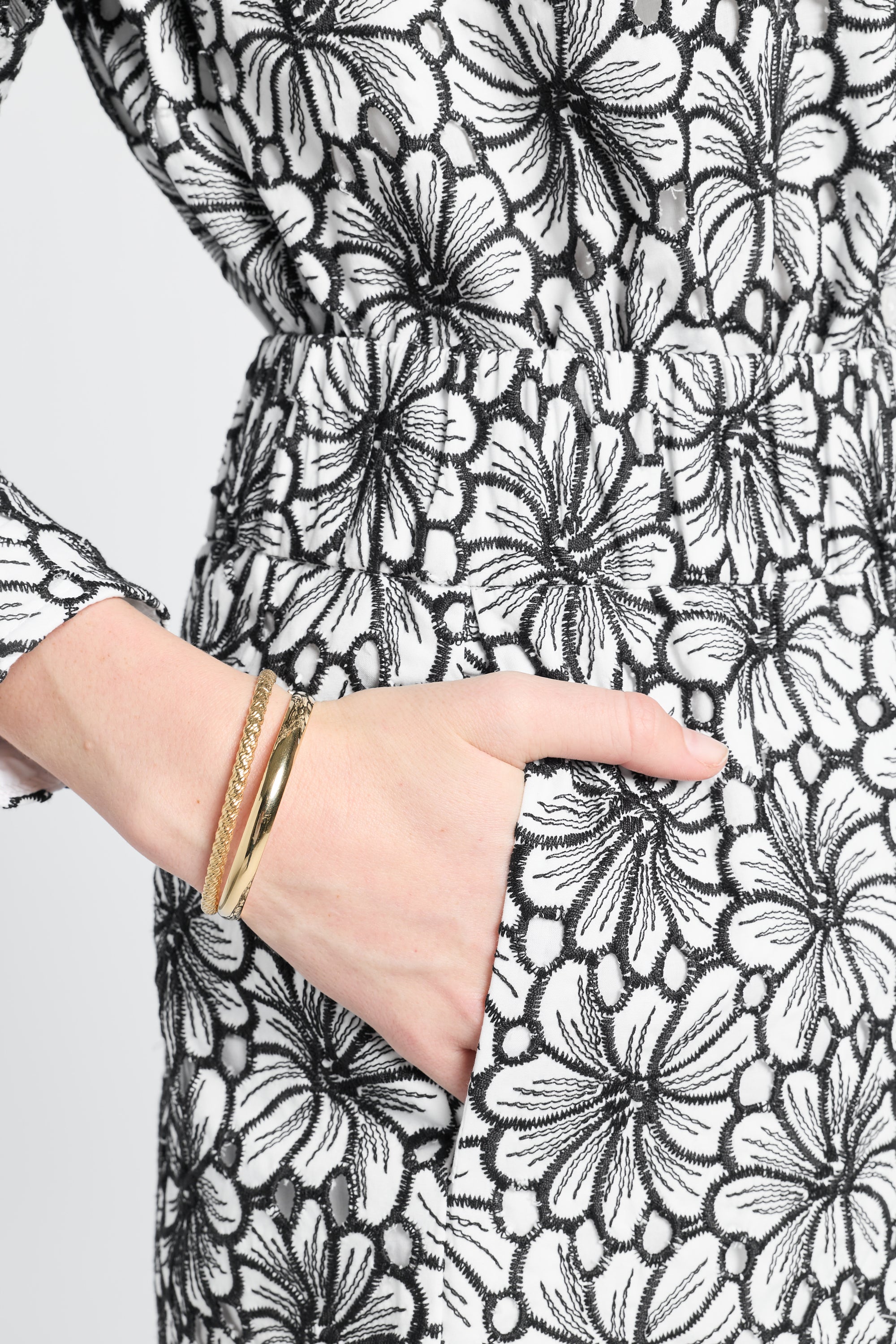 Close-up of a hand wearing a gold bracelet on black and white floral shorts.
