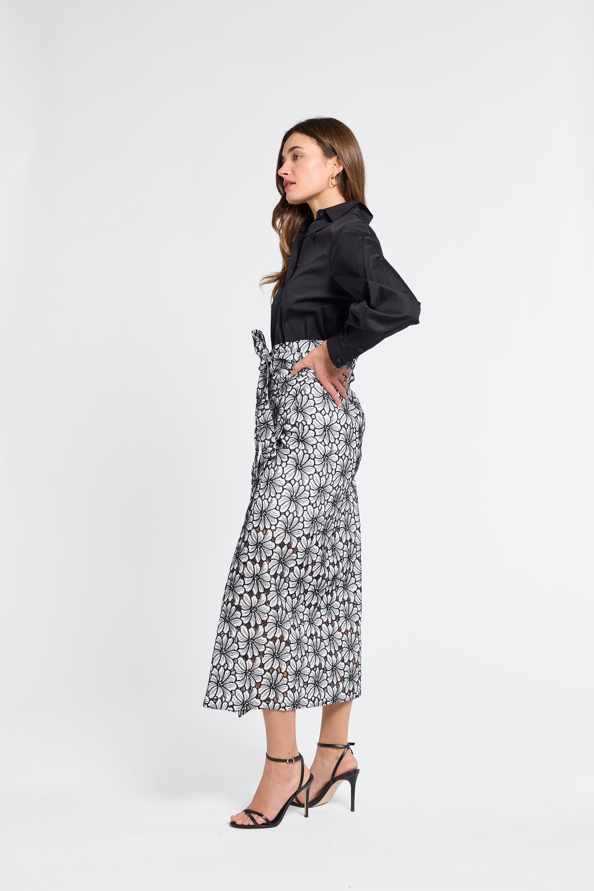 Woman wearing a black blouse and floral black and white embroidered skirt on a white background
