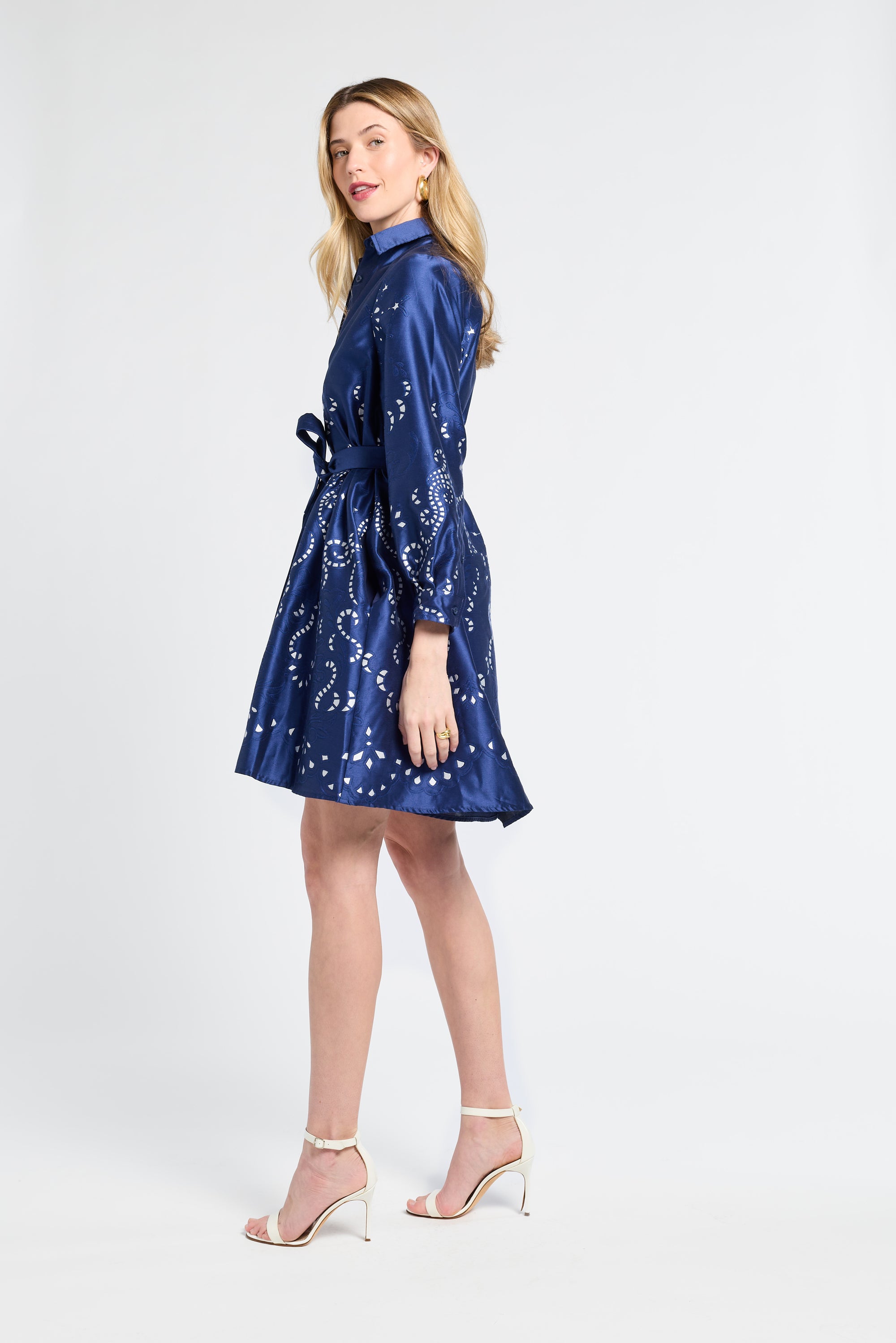 Woman modeling a long sleeve button down navy dress wearing white heels against a white backdrop
