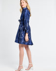 Woman modeling a long sleeve button down navy dress wearing white heels against a white backdrop