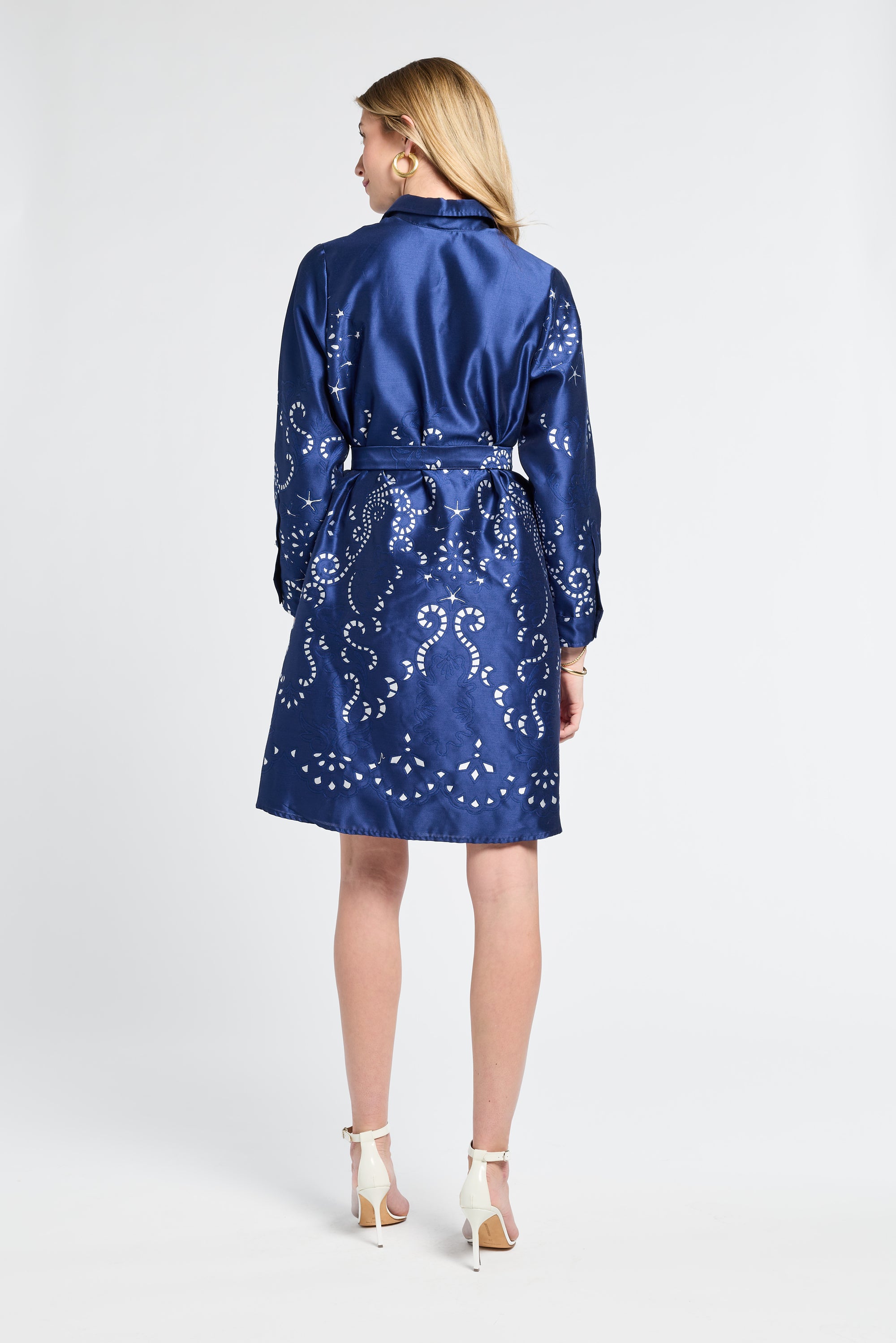 Woman wearing a knee-length navy dress with a silver swirl pattern on a white backdrop