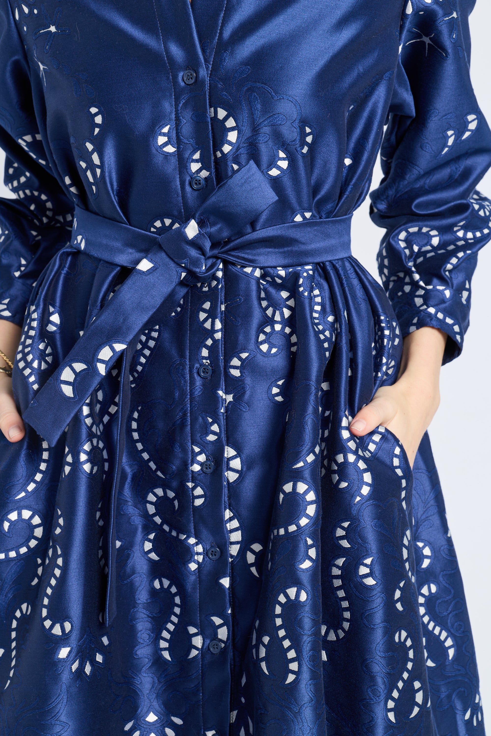 Image of a woman modeling a long sleeve blue dress with silver swirl patterns on a gray backdrop