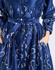 Image of a woman modeling a long sleeve blue dress with silver swirl patterns on a gray backdrop