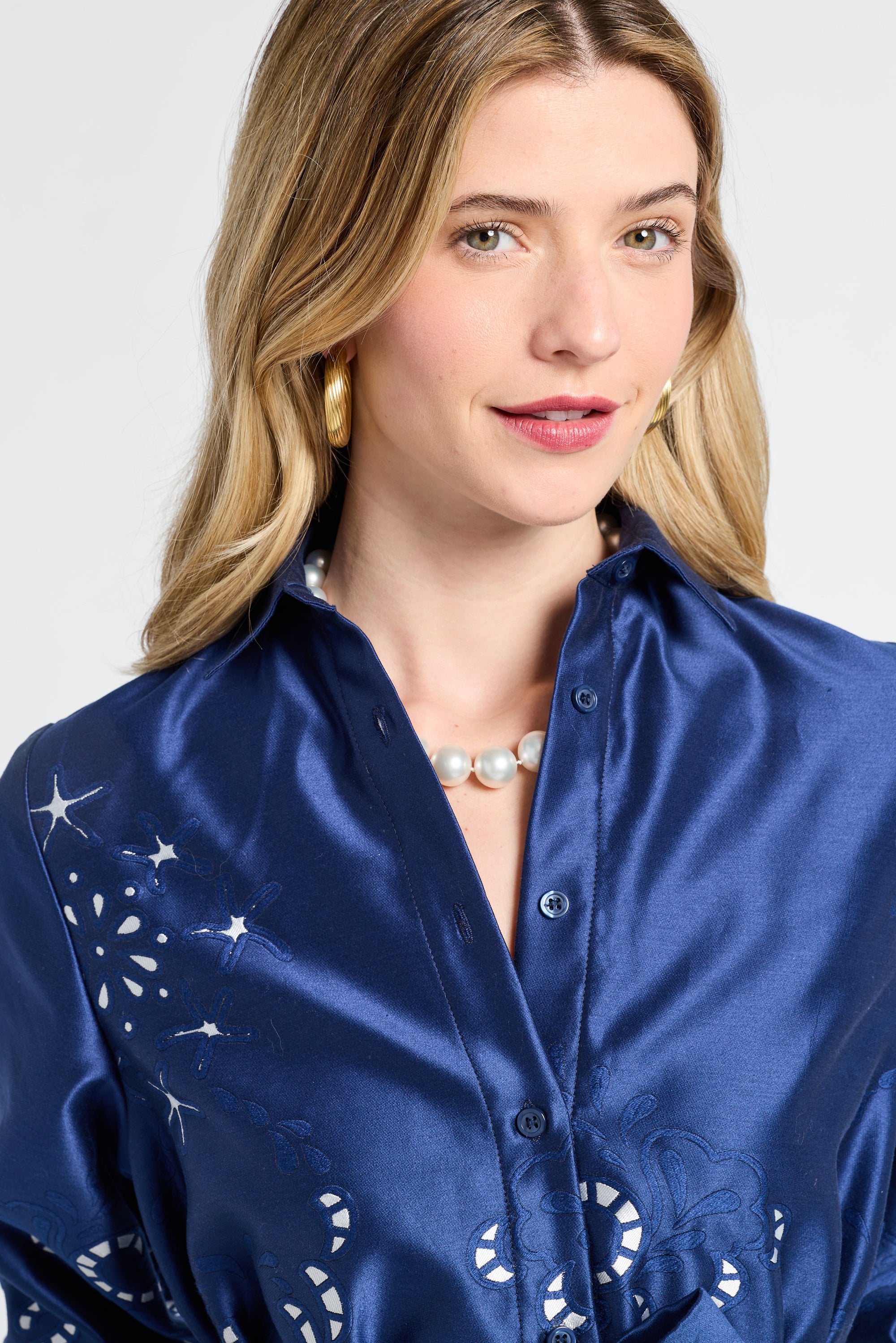 Woman wearing a navy satin dress with silver patterns on a plain background