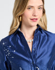 Woman wearing a navy satin dress with silver patterns on a plain background
