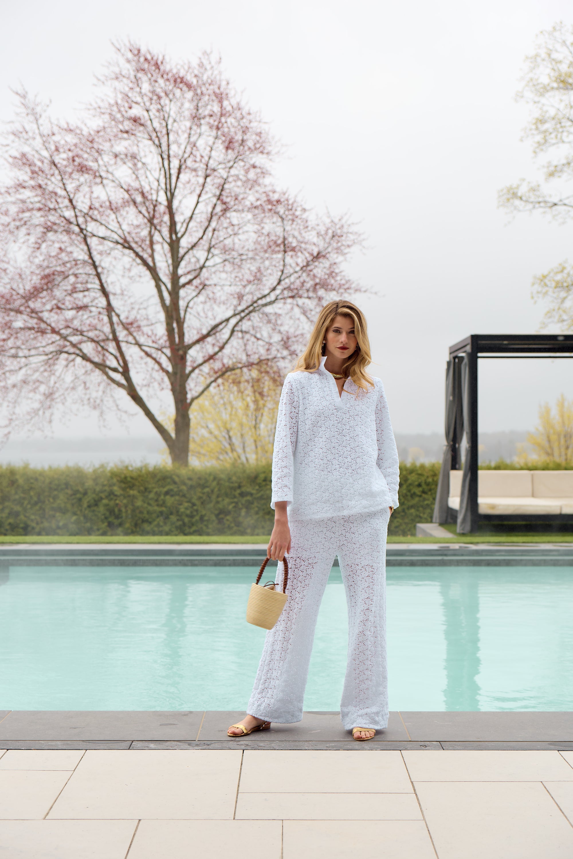 Woman modeling a white lace blouse and pants in front of a swimming pool