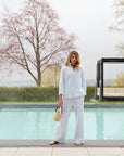 Woman modeling a white lace blouse and pants in front of a swimming pool