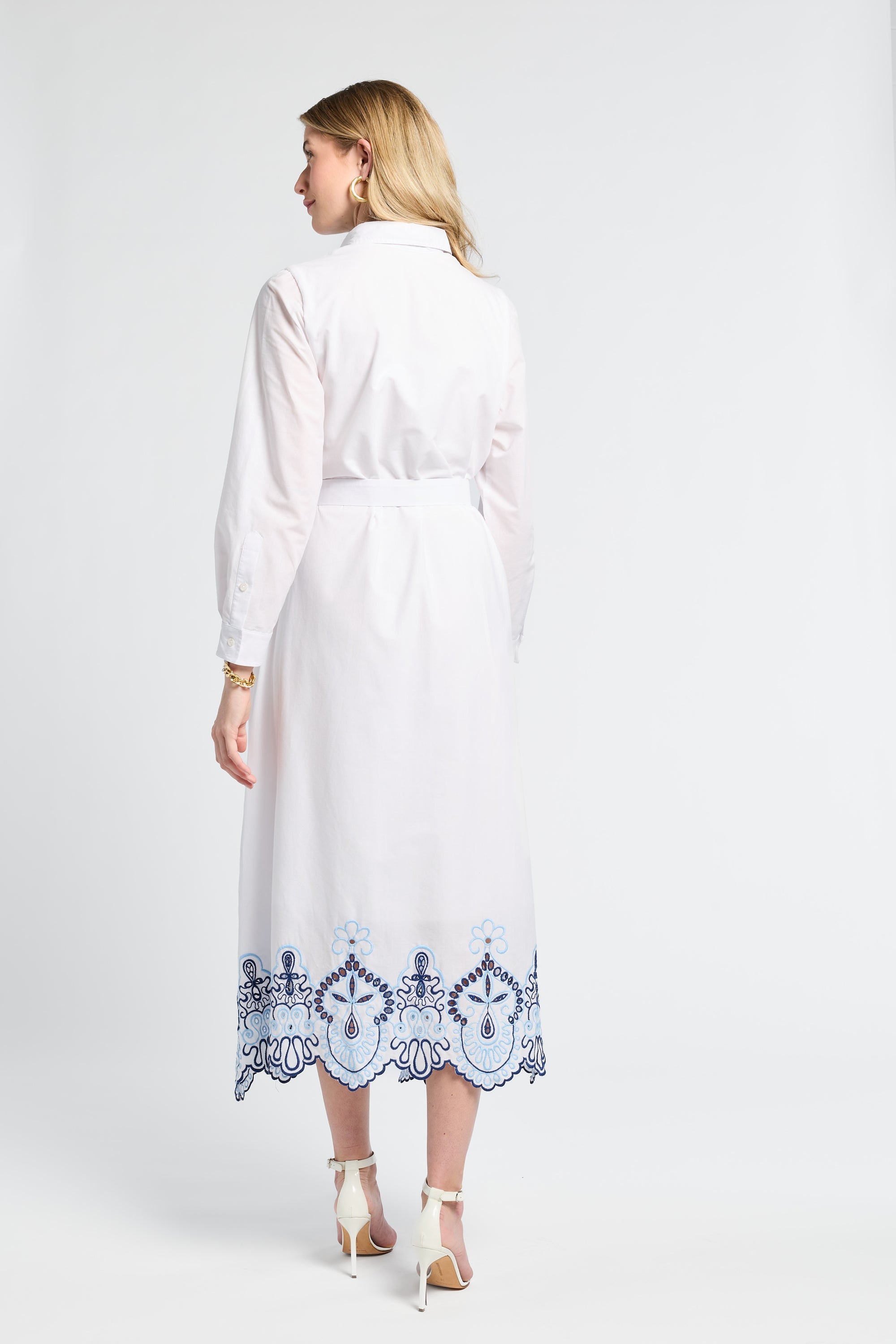 Woman modeling a white dress with blue embroidery on the trim on a plain background