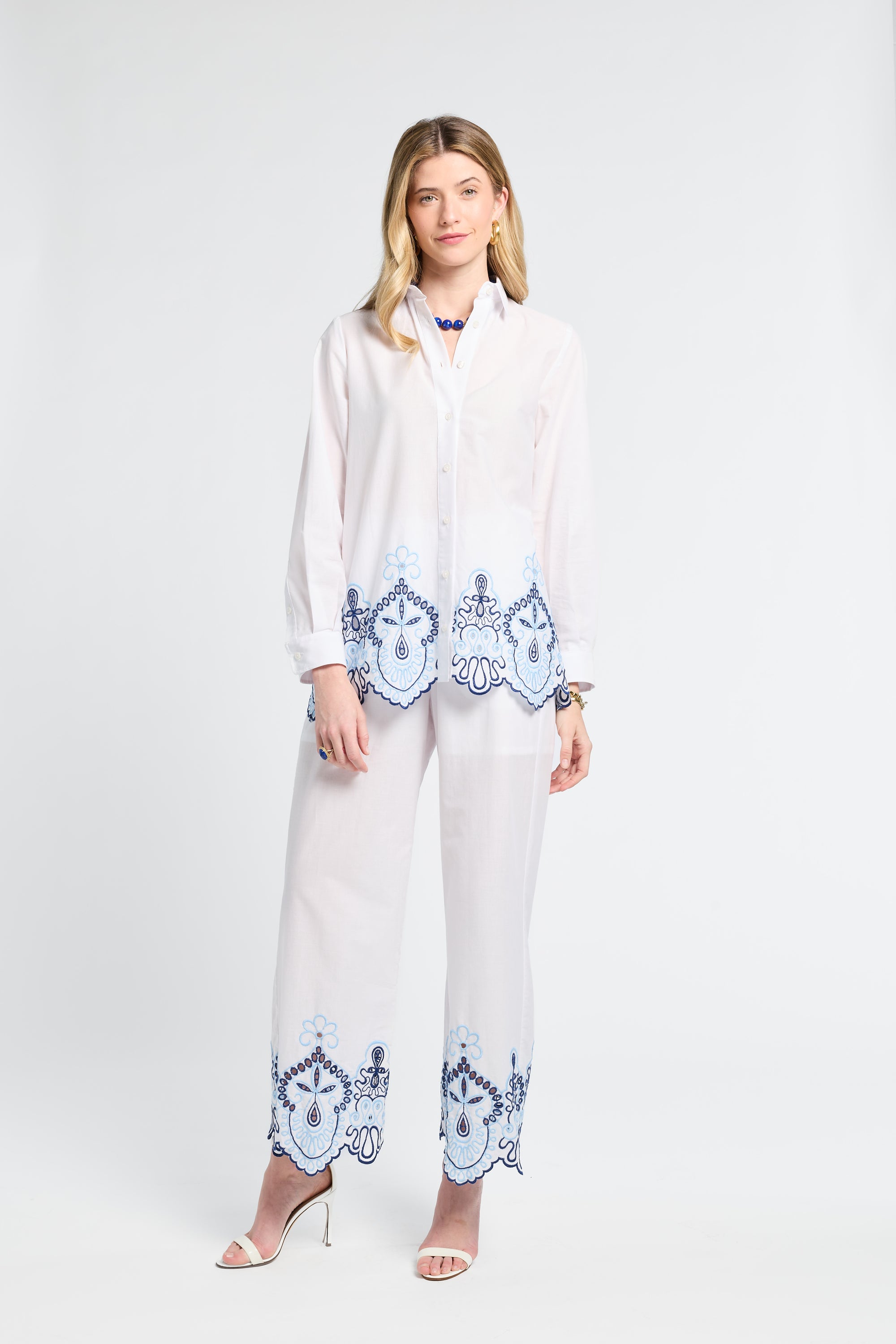 Woman wearing a white blouse and pants with blue embroidery on the trip with a white background