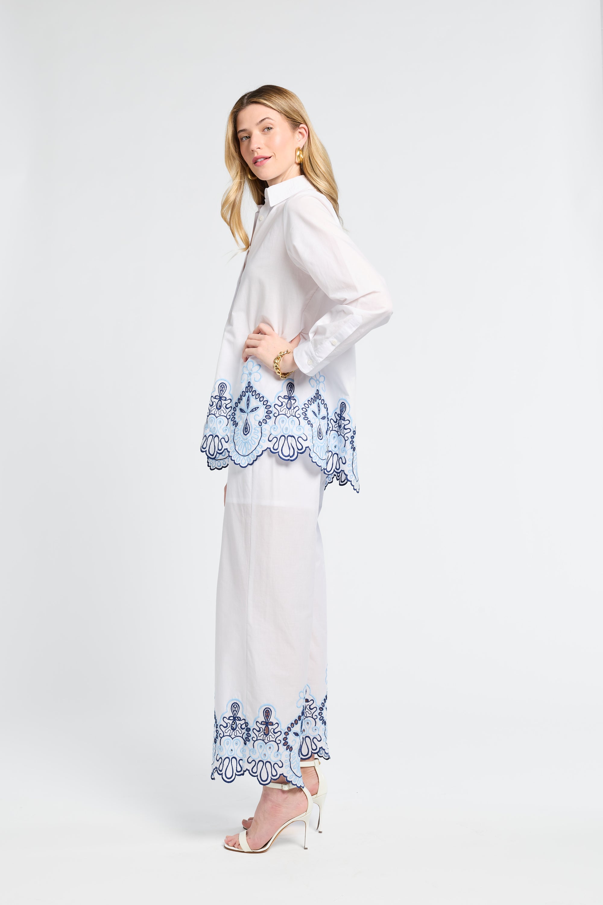 Woman wearing a white blouse and pants with blue lace details on a white background