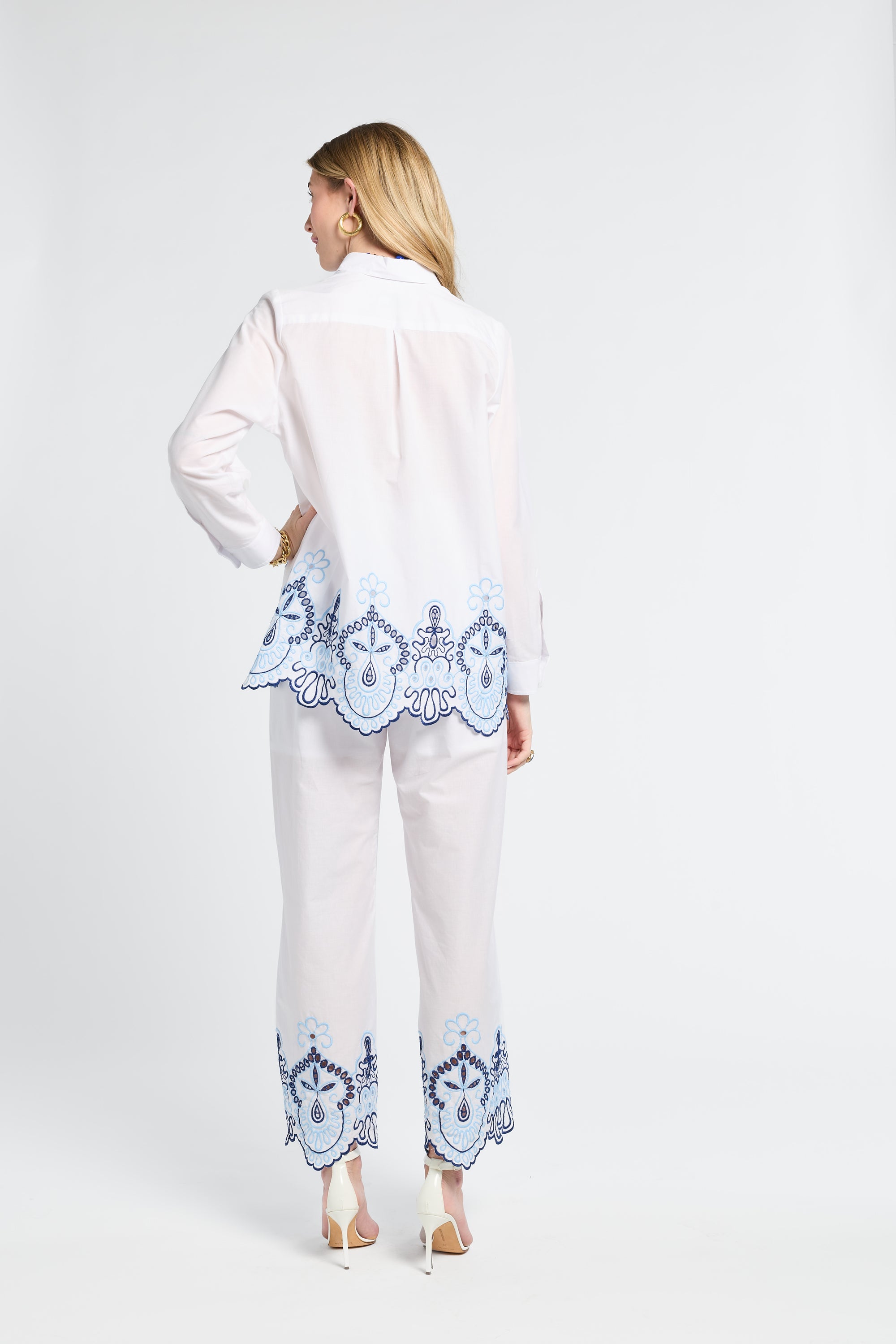 Woman modeling a white blouse and pants with blue lace details on a white background