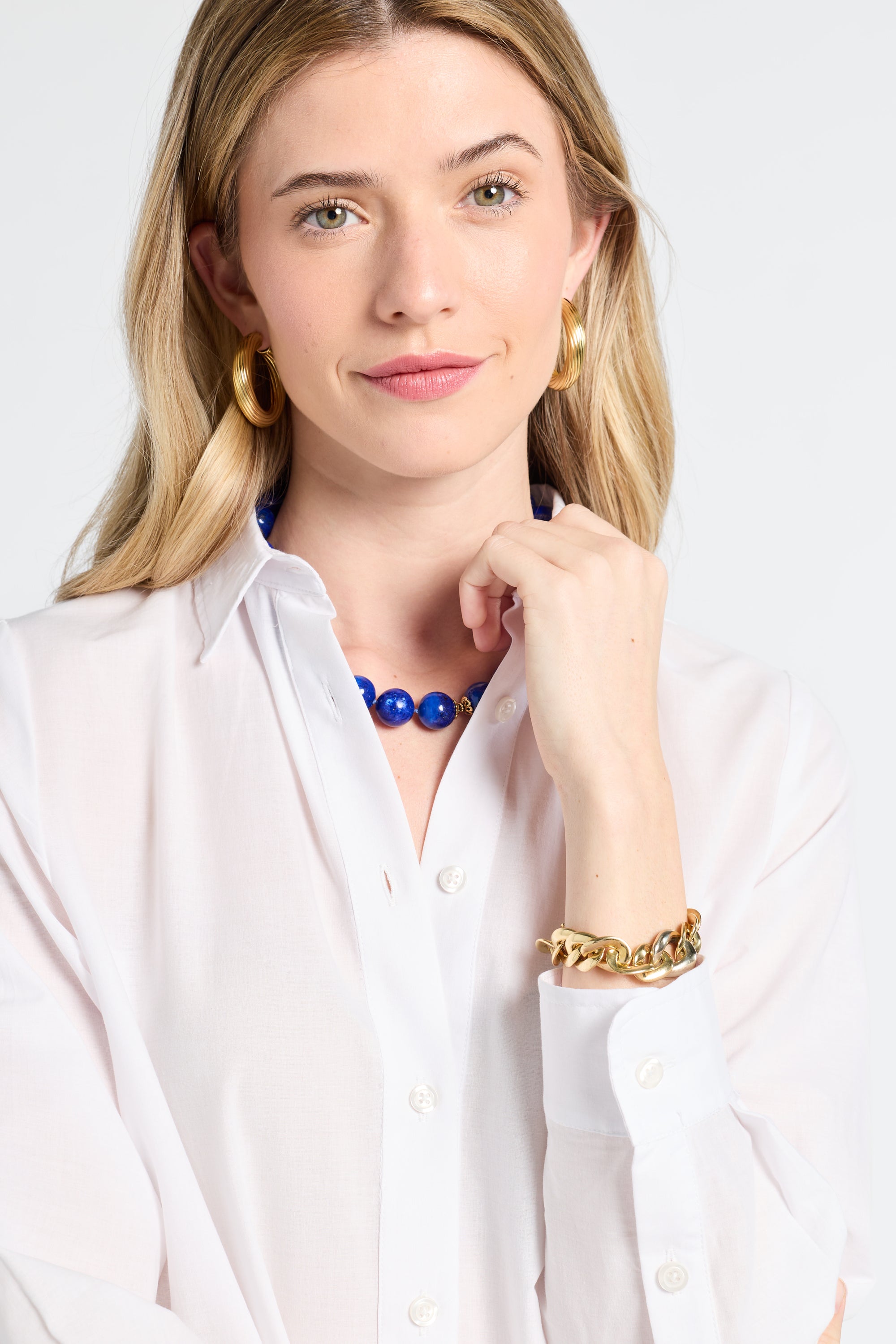 Woman wearing a white blouse with jewelry on a plain background