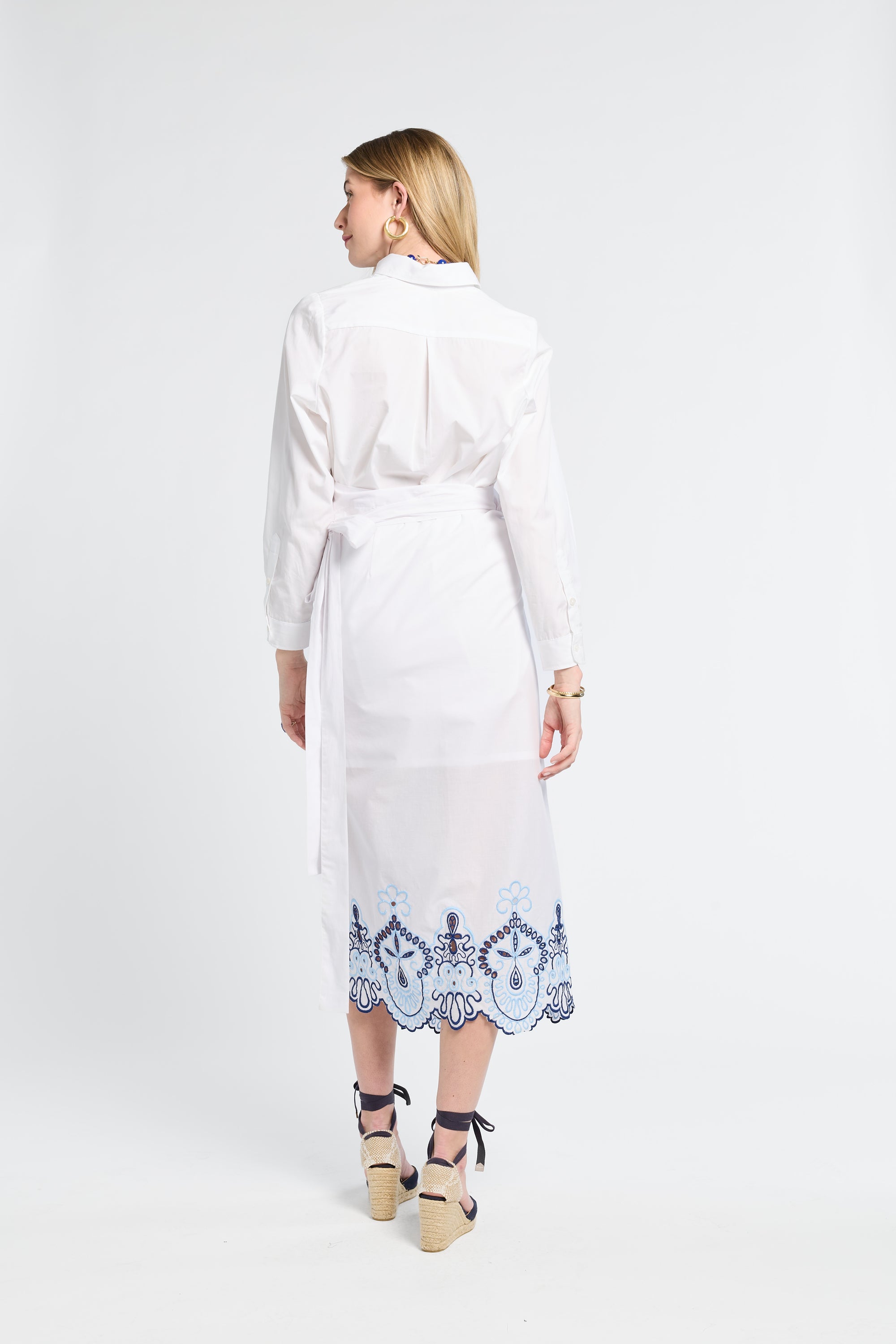 Woman wearing a white blouse and skirt with blue embroidery on a white background