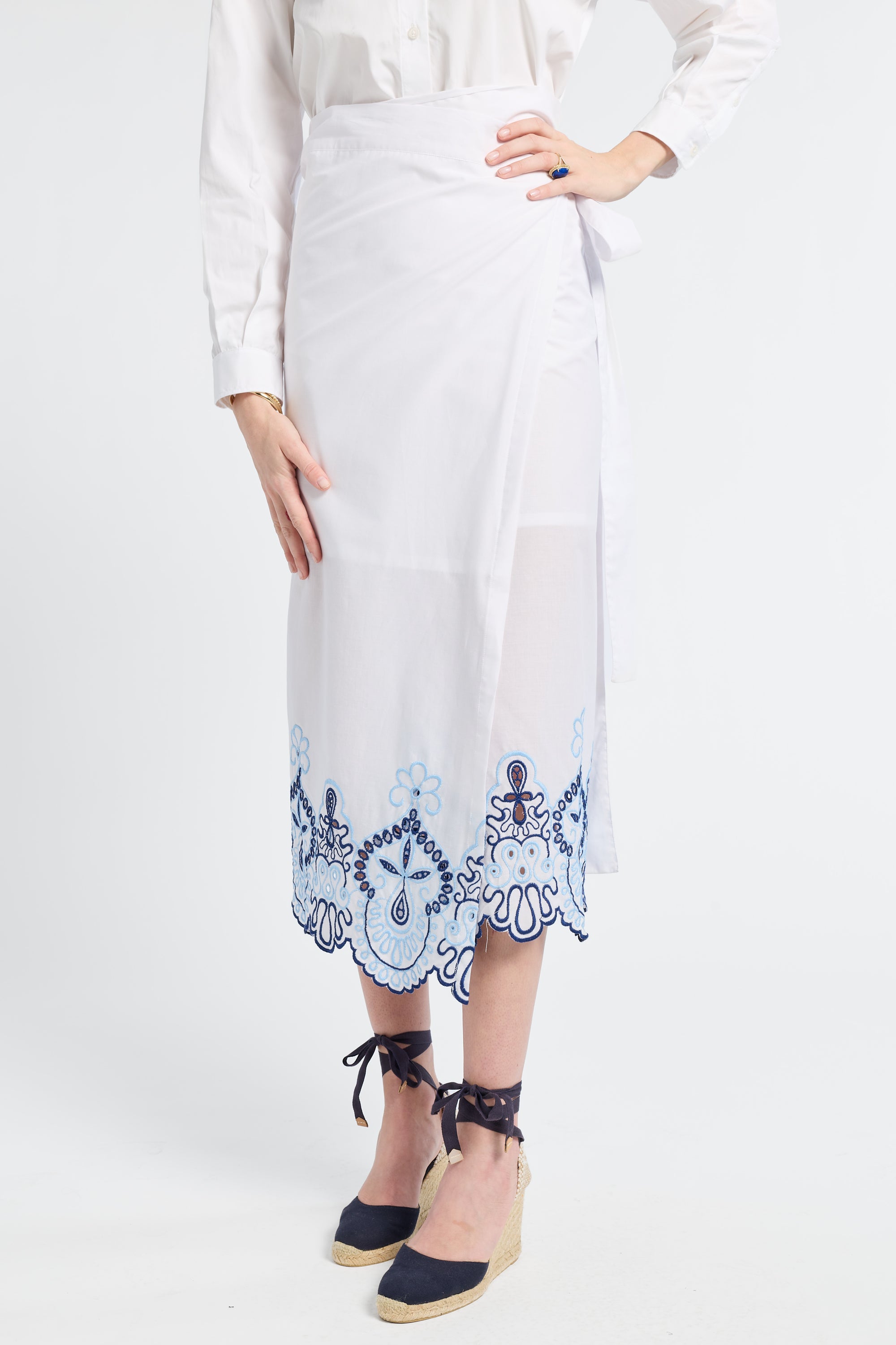 White outfit with a blue patterned white skirt on a plain background