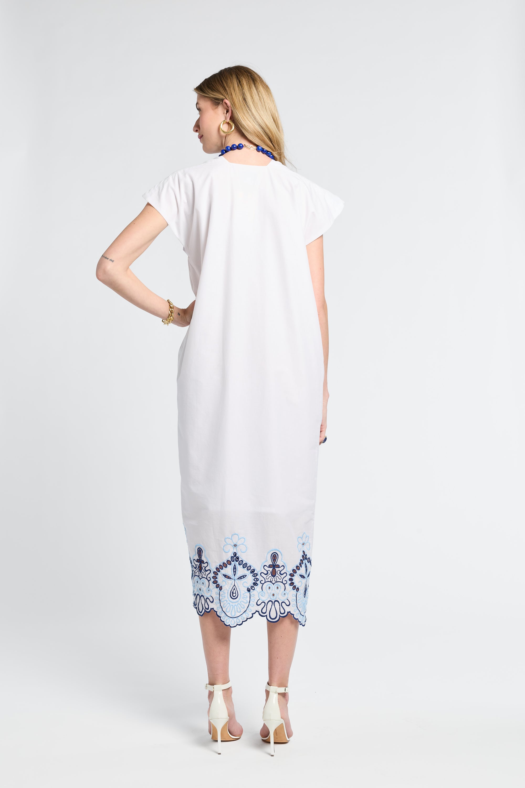 Woman wearing a white dress with blue embroidery details on a plain background