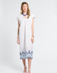 Woman wearing a white caftan with blue lace details on a white background