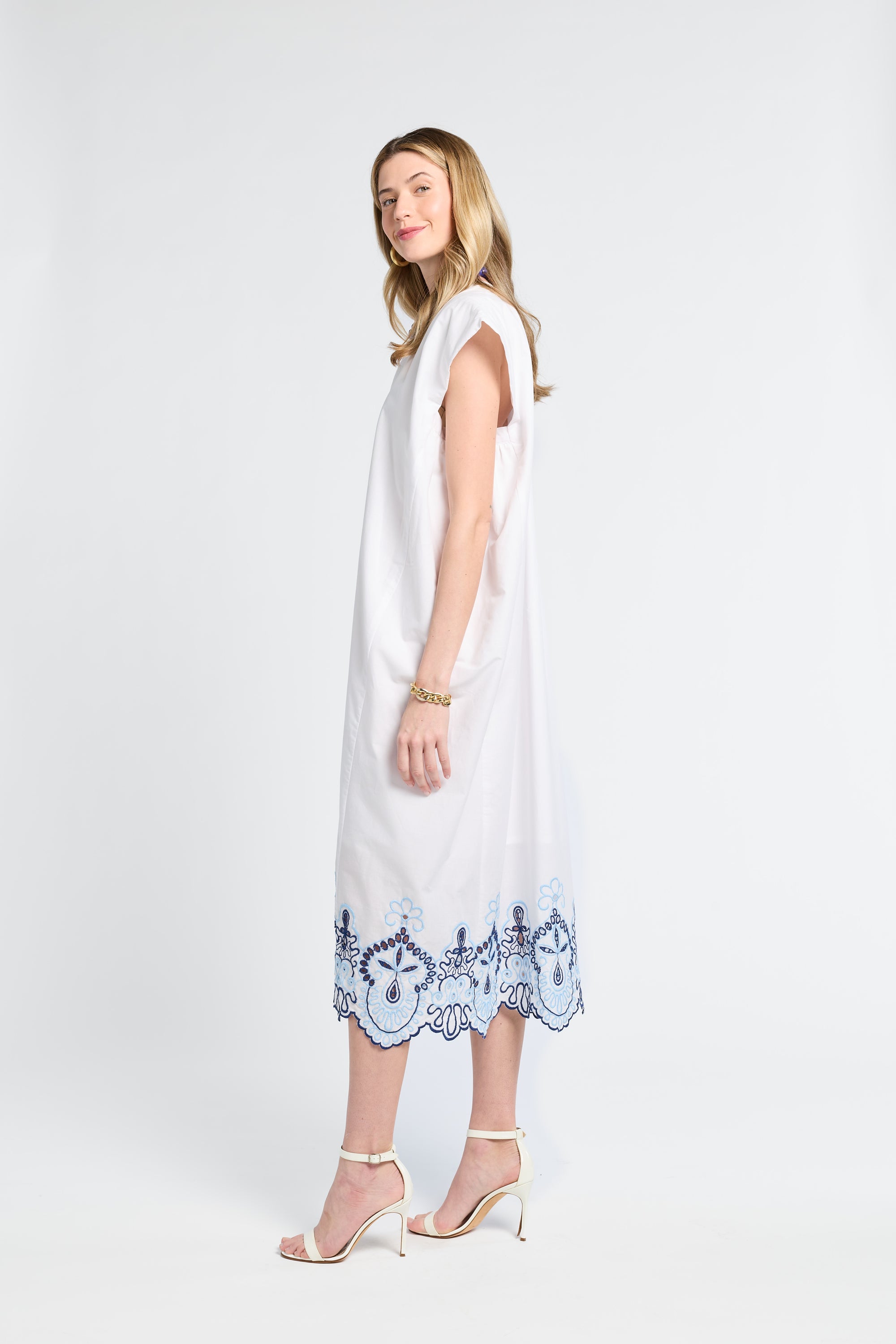 Woman wearing a white dress with blue lace details and white heels on a white background